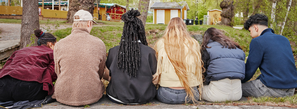 En grupp ungdomar sitter utomhus med ryggen mot kameran.