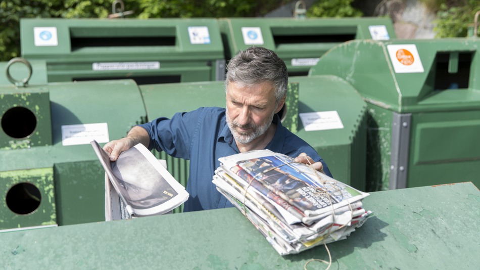 Person slänger tidningar på återvinningsstation.