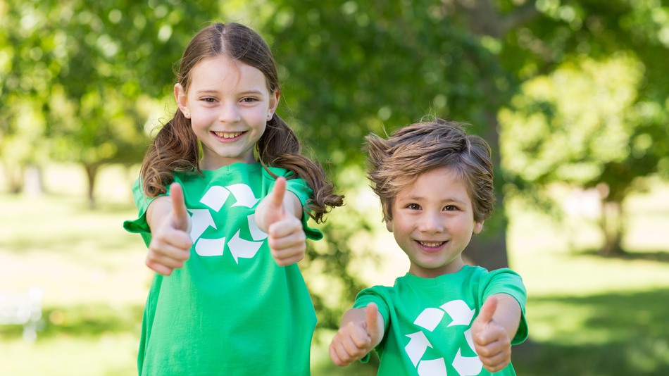 Två barn ler mot kameran och ger tummen upp, iklädda gröna t-shirts med återvinningssymboler på bröstet
